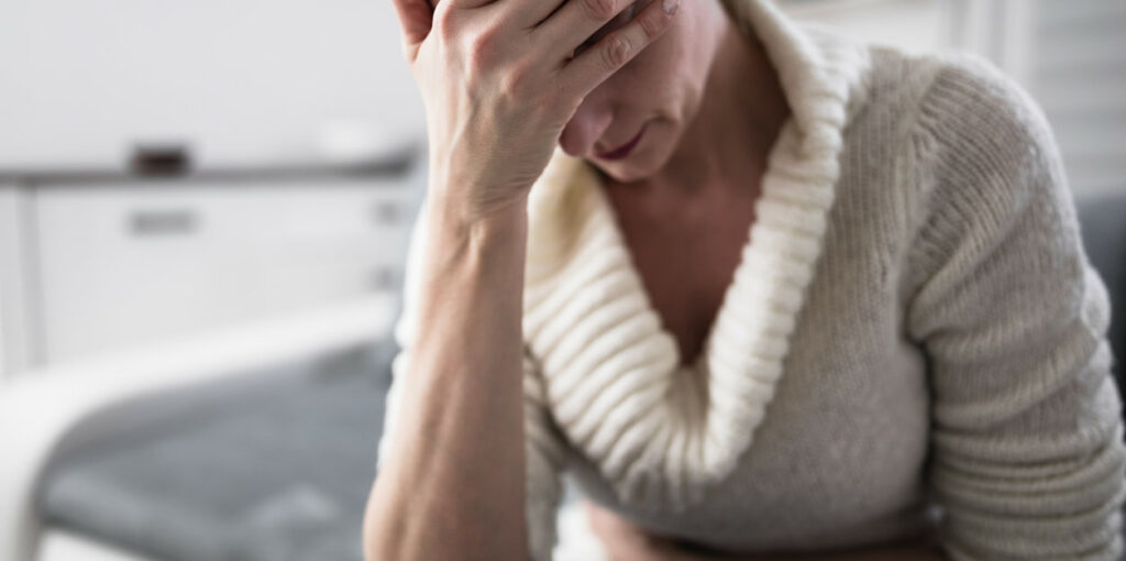 Why Can’t I Drink Alcohol Anymore Without Feeling Sick? An image of a woman holding her stomach with her head resting on her hand. 